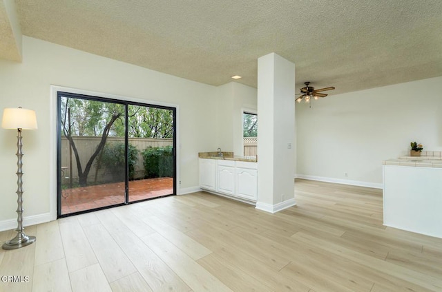 unfurnished living room featuring ceiling fan, a healthy amount of sunlight, light hardwood / wood-style floors, and a textured ceiling