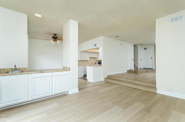 unfurnished living room featuring sink, a textured ceiling, ceiling fan, and light hardwood / wood-style flooring