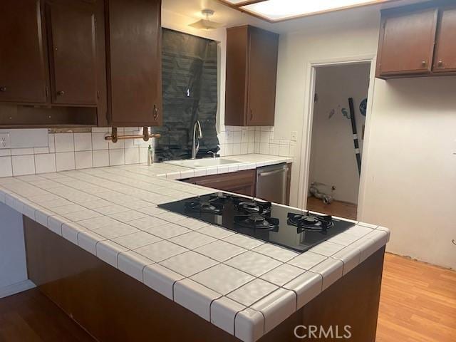 kitchen featuring tile countertops, sink, stainless steel dishwasher, dark brown cabinetry, and light hardwood / wood-style flooring