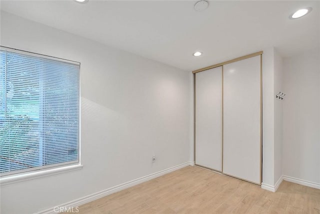 unfurnished bedroom with light wood-type flooring, baseboards, a closet, and recessed lighting