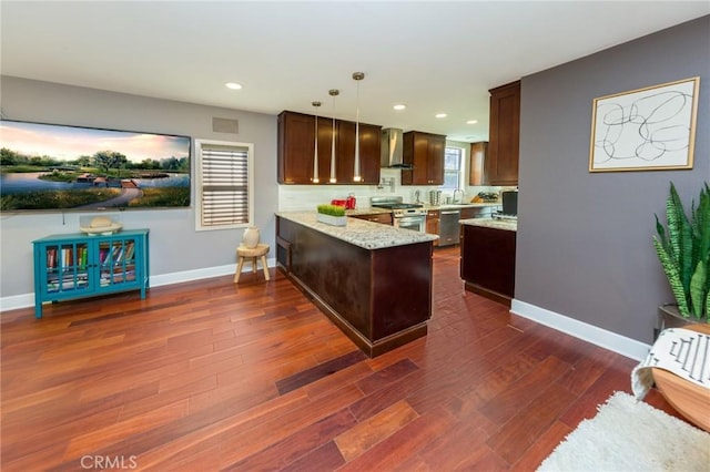 kitchen with hanging light fixtures, appliances with stainless steel finishes, kitchen peninsula, light stone countertops, and wall chimney range hood