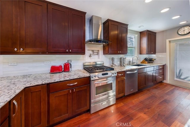 kitchen with appliances with stainless steel finishes, sink, wall chimney range hood, and light stone counters