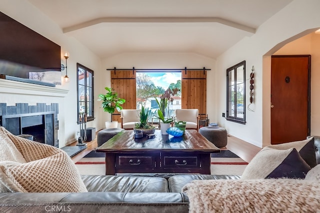 living room with wood-type flooring, a barn door, a tiled fireplace, and vaulted ceiling