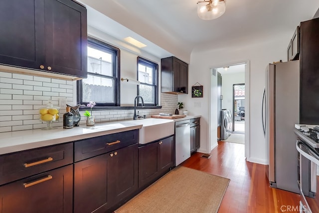 kitchen with dark brown cabinetry, sink, light wood-type flooring, appliances with stainless steel finishes, and decorative backsplash