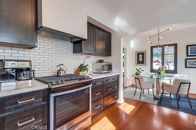 kitchen with appliances with stainless steel finishes, hanging light fixtures, dark brown cabinets, decorative backsplash, and light wood-type flooring