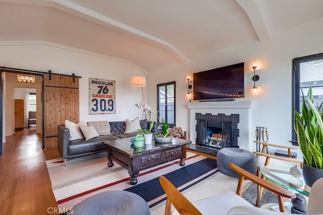 living room with a barn door, vaulted ceiling with beams, hardwood / wood-style floors, and a fireplace