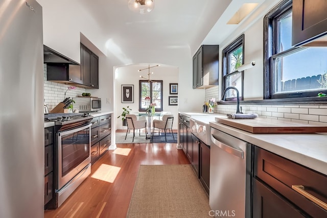 kitchen featuring sink, light hardwood / wood-style flooring, hanging light fixtures, stainless steel appliances, and tasteful backsplash