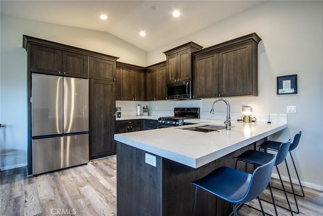 kitchen featuring vaulted ceiling, appliances with stainless steel finishes, sink, a kitchen breakfast bar, and kitchen peninsula