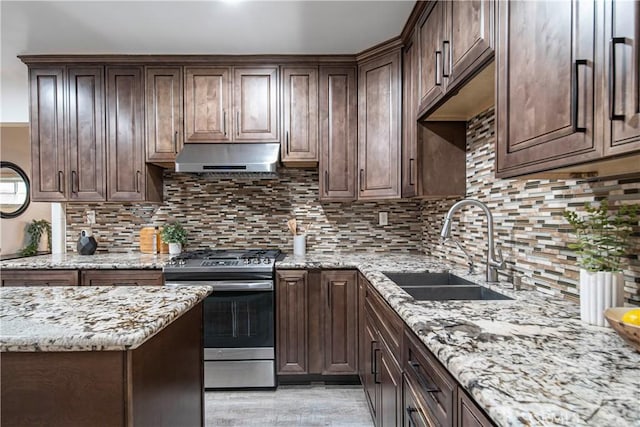 kitchen with sink, dark brown cabinets, stainless steel range with gas cooktop, light stone countertops, and decorative backsplash