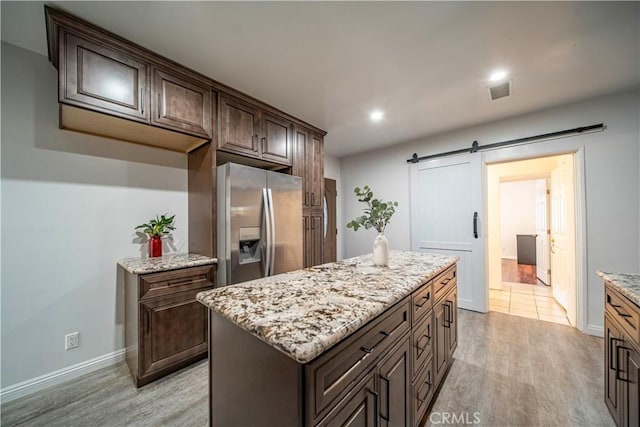 kitchen featuring dark brown cabinets, stainless steel refrigerator with ice dispenser, light hardwood / wood-style floors, a kitchen island, and a barn door