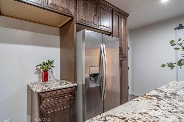 kitchen featuring dark brown cabinetry, light stone counters, and stainless steel refrigerator with ice dispenser