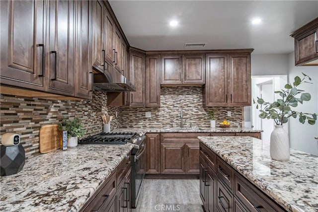 kitchen with sink, gas stove, dark brown cabinets, light stone countertops, and backsplash