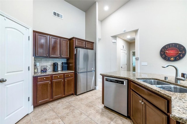 kitchen featuring appliances with stainless steel finishes, sink, decorative backsplash, a high ceiling, and light stone countertops