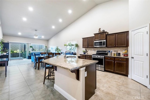 kitchen with sink, a breakfast bar, appliances with stainless steel finishes, light stone counters, and a center island with sink