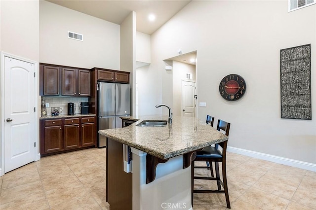 kitchen featuring sink, a breakfast bar area, stainless steel refrigerator, an island with sink, and light stone countertops