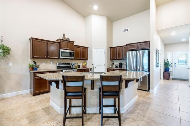 kitchen with sink, a breakfast bar, a kitchen island with sink, stainless steel appliances, and light stone counters