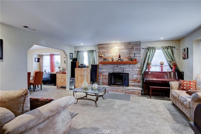 carpeted living room with a stone fireplace and plenty of natural light