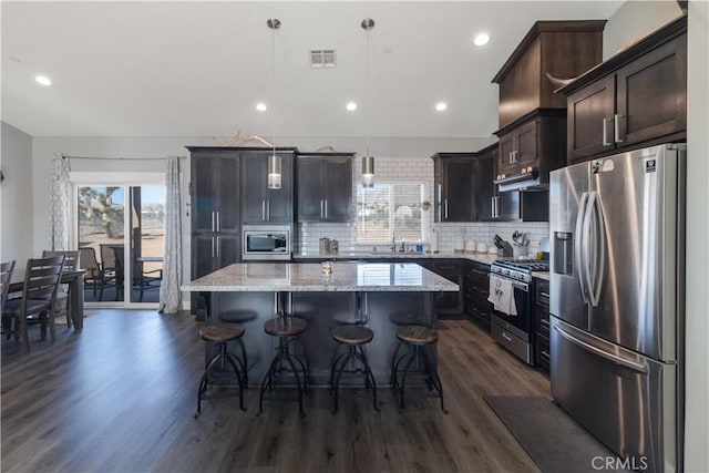 kitchen featuring appliances with stainless steel finishes, decorative light fixtures, a kitchen breakfast bar, a center island, and light stone countertops