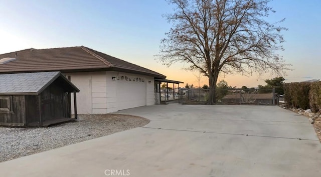 view of side of property with fence, driveway, stucco siding, a garage, and a tiled roof