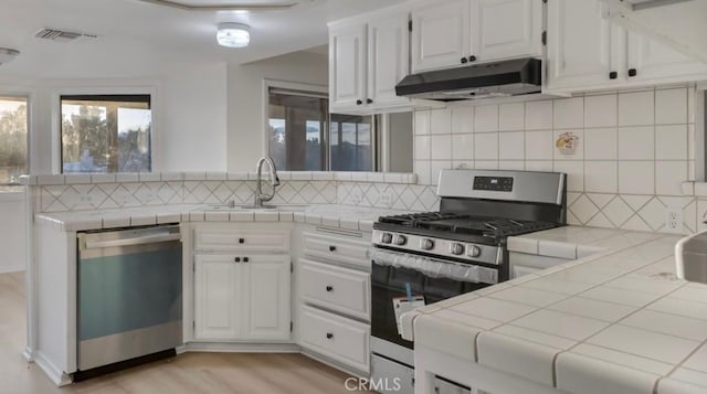 kitchen featuring visible vents, under cabinet range hood, a sink, appliances with stainless steel finishes, and tile counters