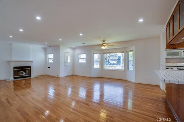 unfurnished living room with ceiling fan, a wealth of natural light, and light wood-type flooring