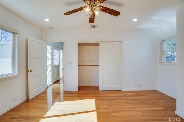 unfurnished bedroom with multiple windows, ceiling fan, light wood-type flooring, and a closet