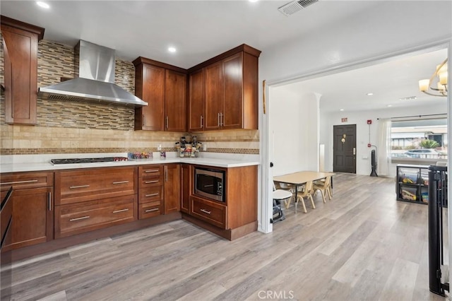 kitchen with appliances with stainless steel finishes, wall chimney range hood, decorative backsplash, and light hardwood / wood-style flooring