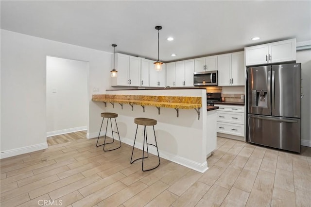 kitchen with a kitchen bar, hanging light fixtures, kitchen peninsula, stainless steel appliances, and white cabinets