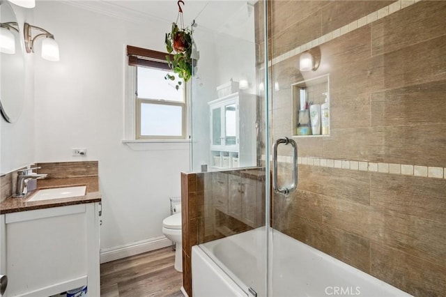 full bathroom featuring toilet, crown molding, bath / shower combo with glass door, vanity, and hardwood / wood-style flooring