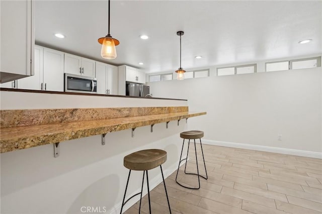 kitchen featuring white cabinetry, hanging light fixtures, stainless steel appliances, a kitchen breakfast bar, and kitchen peninsula