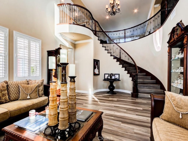 living area with a chandelier, a high ceiling, wood finished floors, baseboards, and stairs