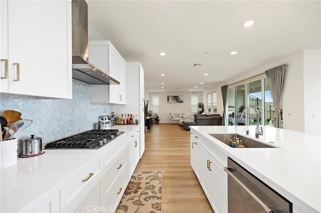 kitchen featuring appliances with stainless steel finishes, sink, white cabinets, light hardwood / wood-style floors, and wall chimney range hood