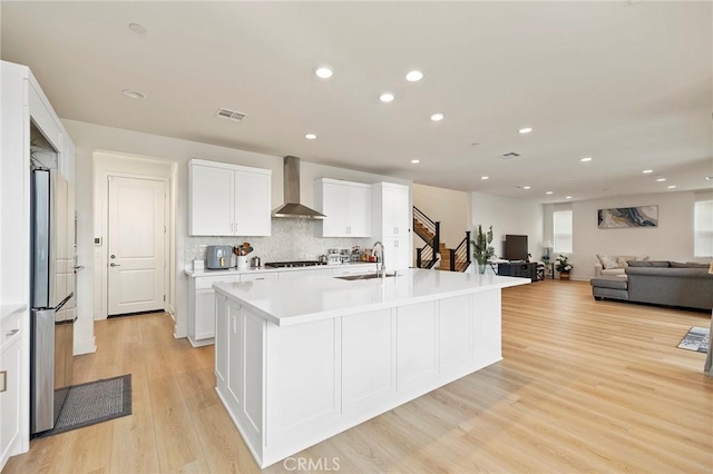 kitchen with white cabinetry, sink, wall chimney exhaust hood, a center island with sink, and light hardwood / wood-style flooring