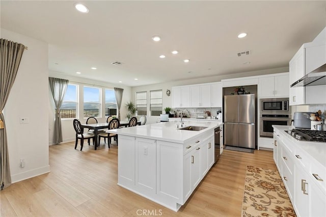 kitchen featuring sink, light hardwood / wood-style flooring, a center island with sink, stainless steel appliances, and white cabinets