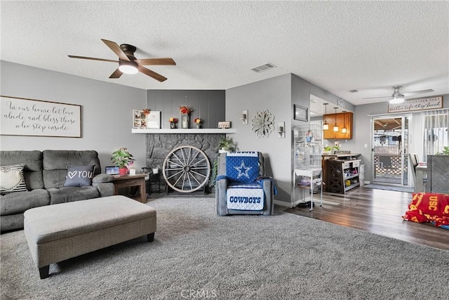 living room with dark wood-type flooring, ceiling fan, a stone fireplace, and a textured ceiling