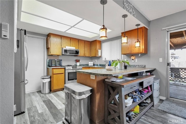 kitchen with a peninsula, a kitchen breakfast bar, light countertops, appliances with stainless steel finishes, and decorative light fixtures