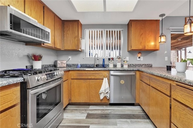 kitchen with stainless steel appliances, hanging light fixtures, sink, and light hardwood / wood-style flooring