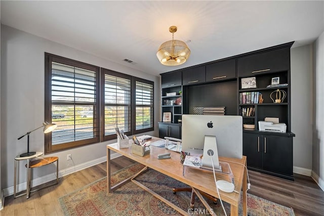 office with built in shelves, wood-type flooring, and a notable chandelier