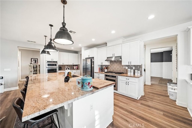 kitchen featuring a breakfast bar area, hanging light fixtures, stainless steel appliances, white cabinets, and a large island with sink