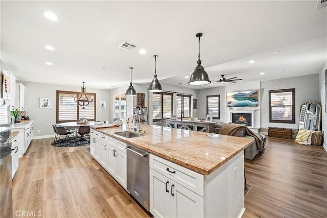 kitchen with decorative light fixtures, white cabinets, a kitchen island with sink, stainless steel dishwasher, and light stone countertops