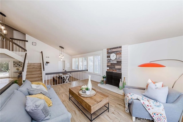 living room with high vaulted ceiling, a fireplace, and light hardwood / wood-style floors