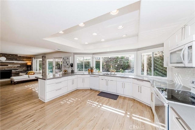 kitchen with white appliances, light hardwood / wood-style flooring, a raised ceiling, and white cabinets