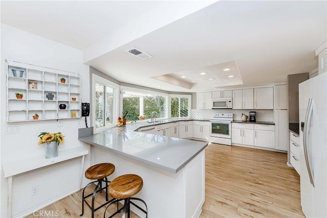 kitchen with a raised ceiling, white cabinetry, white appliances, and kitchen peninsula