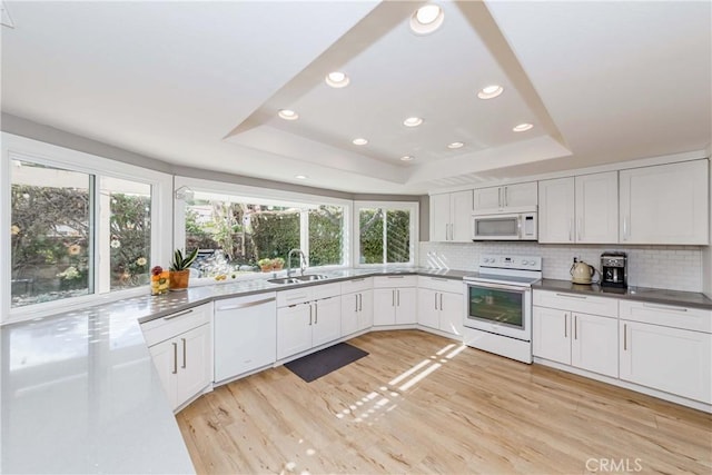 kitchen with tasteful backsplash, white appliances, a raised ceiling, and white cabinets