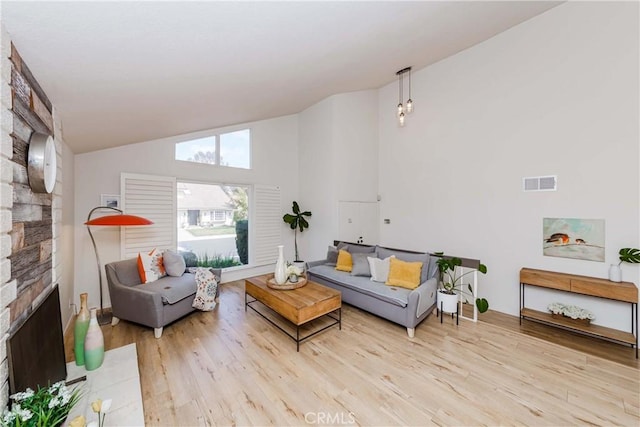 living room with a stone fireplace, light hardwood / wood-style flooring, and high vaulted ceiling