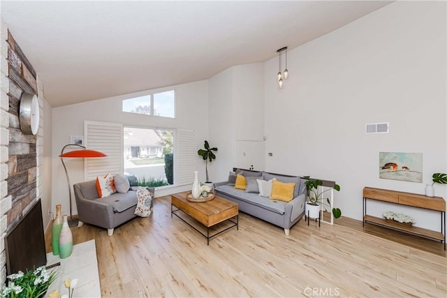 living area with high vaulted ceiling, visible vents, a stone fireplace, and light wood finished floors