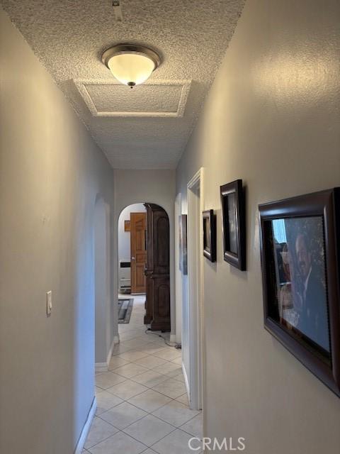 corridor featuring a textured ceiling and light tile patterned flooring