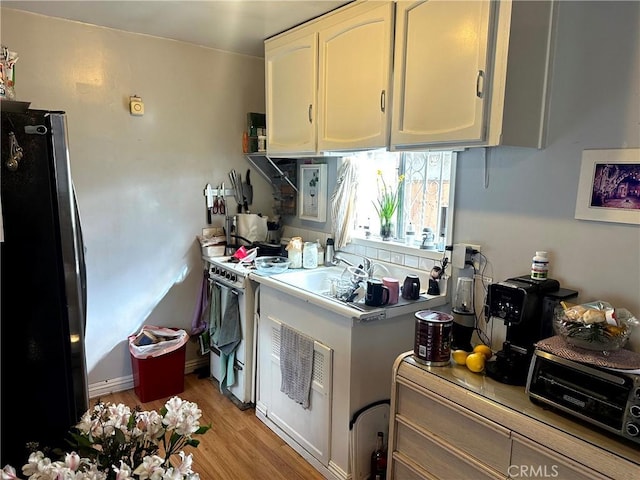 kitchen with white range with gas cooktop, refrigerator, light hardwood / wood-style flooring, and white cabinets