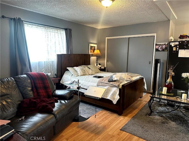 bedroom with black refrigerator, light hardwood / wood-style floors, a closet, and a textured ceiling