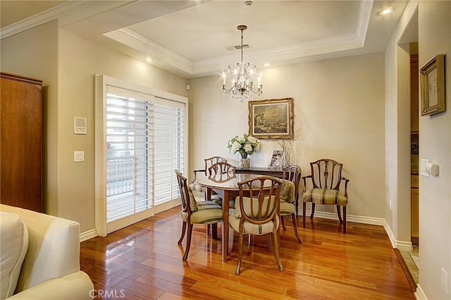 dining area with crown molding, hardwood / wood-style floors, a tray ceiling, and a chandelier